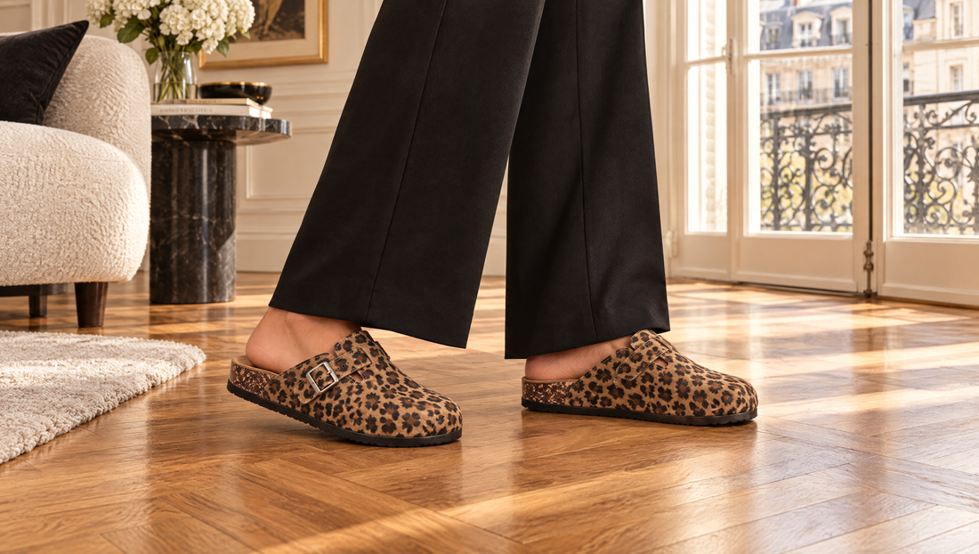 Pieds en mules imprimé léopard en velours vegan avec un pantalon noir large sur un parquet en chevrons